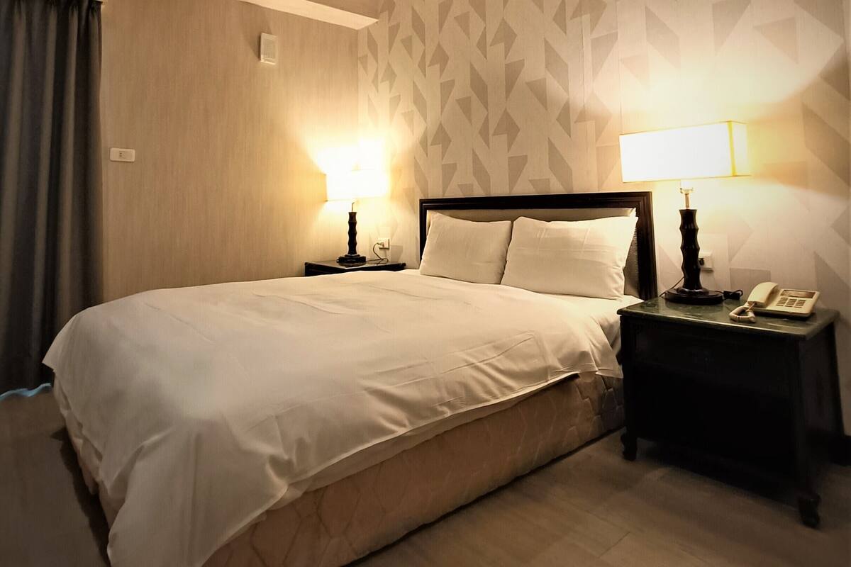 Une chambre d’hôtel avec un grand lit, deux tables de chevet avec des lampes, un téléphone et un papier peint à motifs.