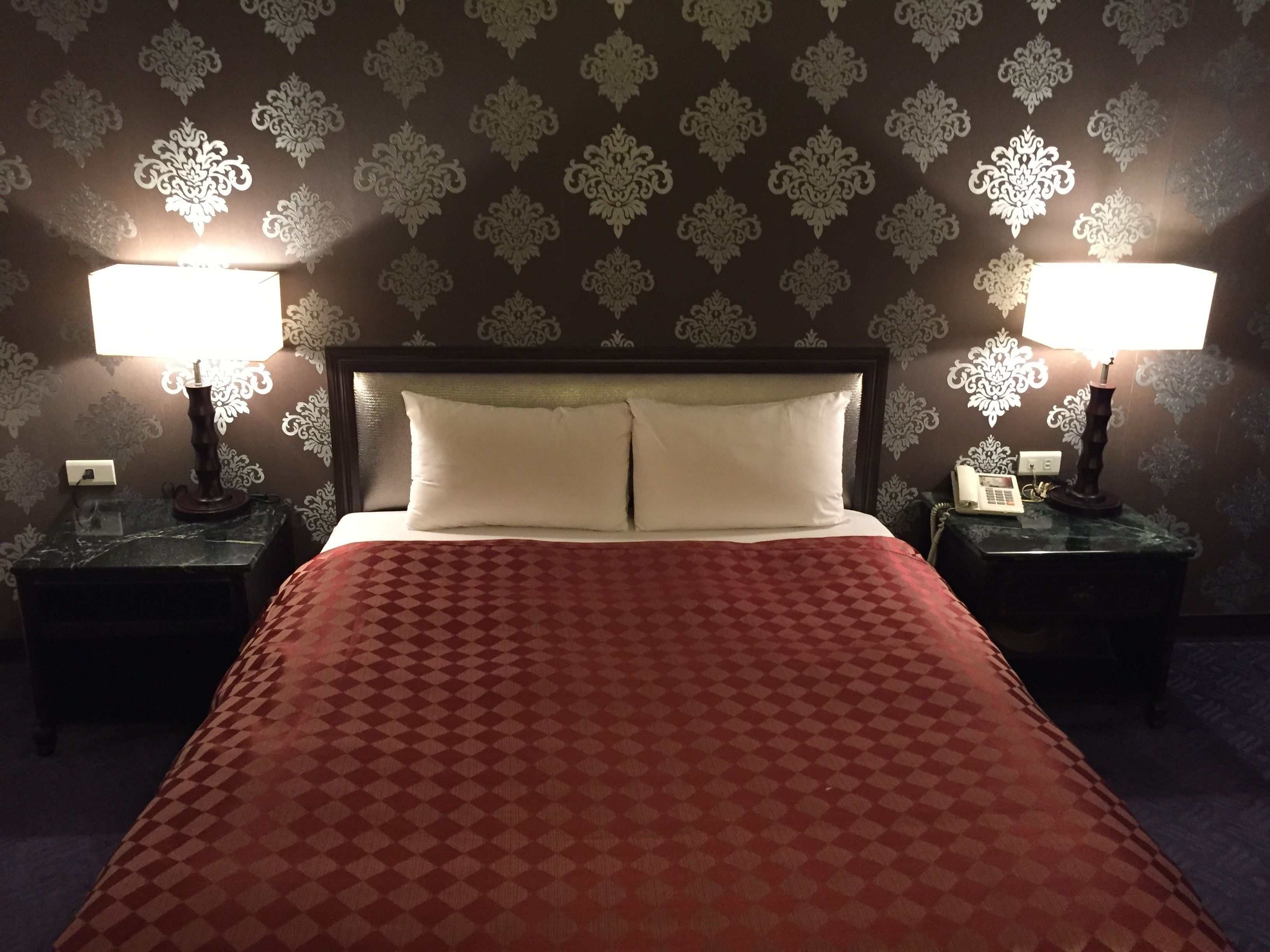 Une chambre d’hôtel avec un grand lit, deux lampes de chevet et un papier peint à motifs.