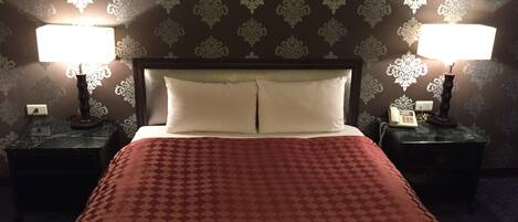 Une chambre d’hôtel avec un grand lit, deux lampes de chevet et un papier peint à motifs.