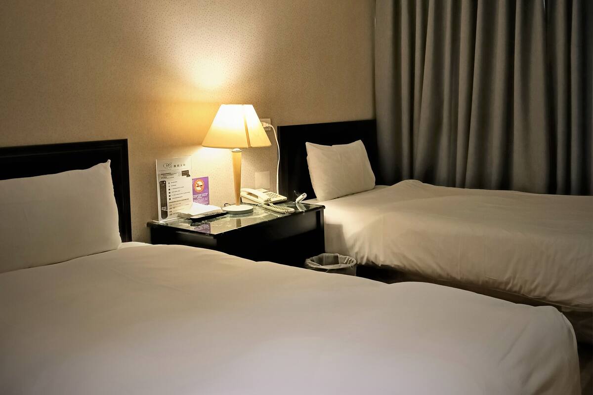 Une chambre d’hôtel avec deux lits, une table de chevet avec une lampe, un téléphone et une poubelle.