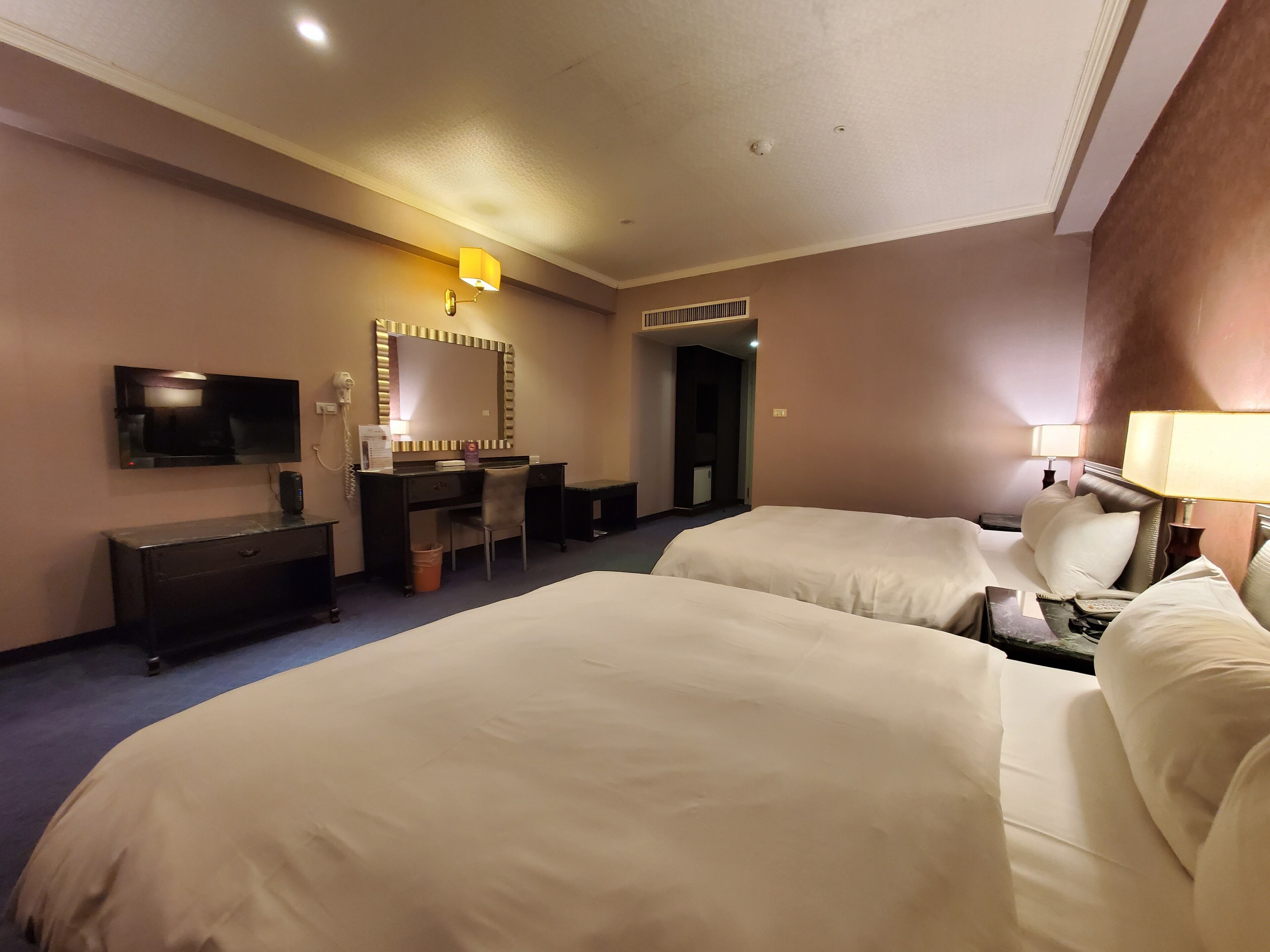 Una habitación de hotel con dos camas, un escritorio con silla, un televisor y un espejo.