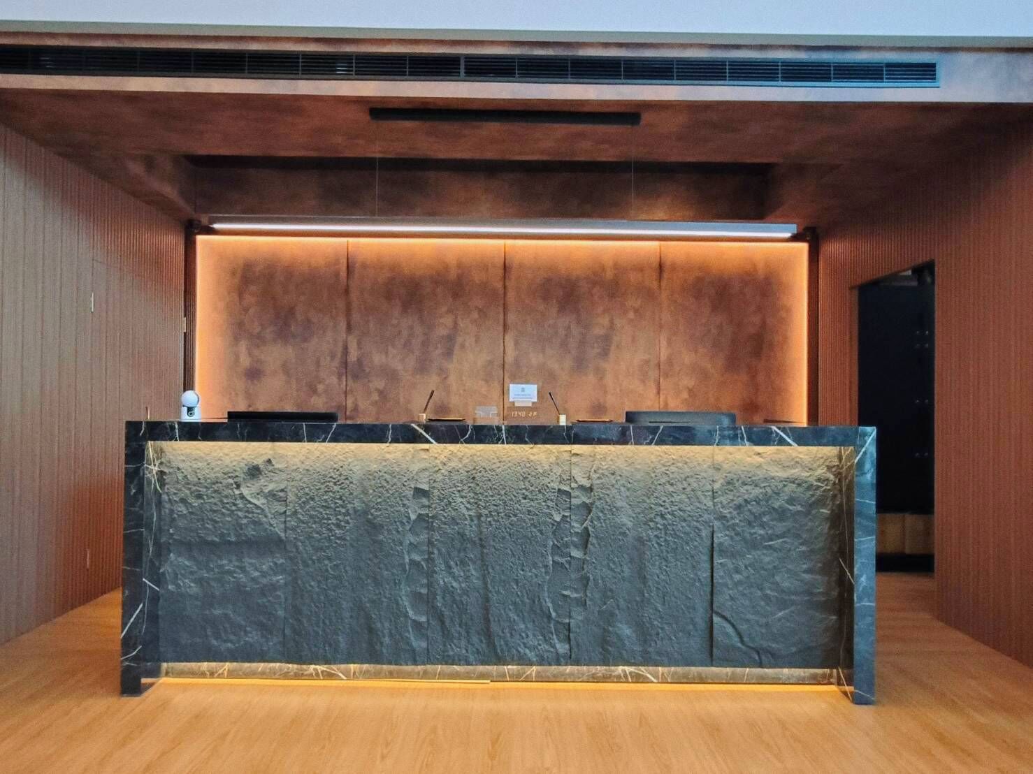 A reception desk with a marble top, wooden paneling on the walls, and a modern light fixture above.
