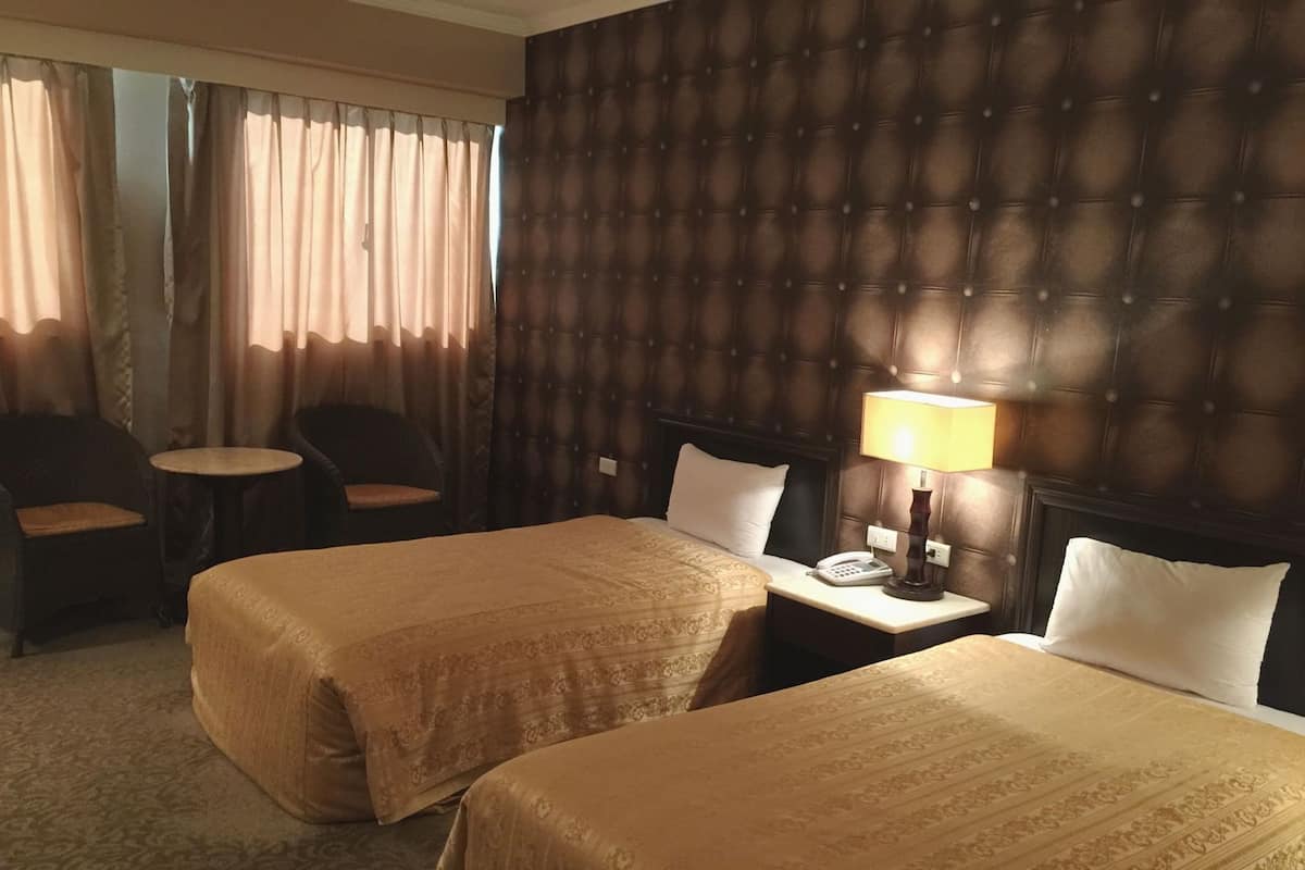 Une chambre d’hôtel avec deux lits, une petite table ronde, deux chaises, une lampe et un téléphone sur une table de chevet.