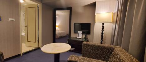 A hotel room with a bed, a TV, a desk, a lamp, and a small table.