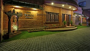 Un hotel con fachada de ladrillo, un cartel que dice "HOTEL DAHLIA PORTARA" y un jardín bien cuidado.