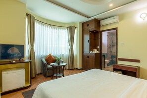 A hotel room with a bed, a TV, a small table with a plant, a sofa, and a wardrobe.