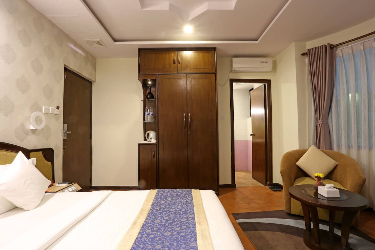 A hotel room with a bed, a wardrobe, a small table with a vase, and a chair.