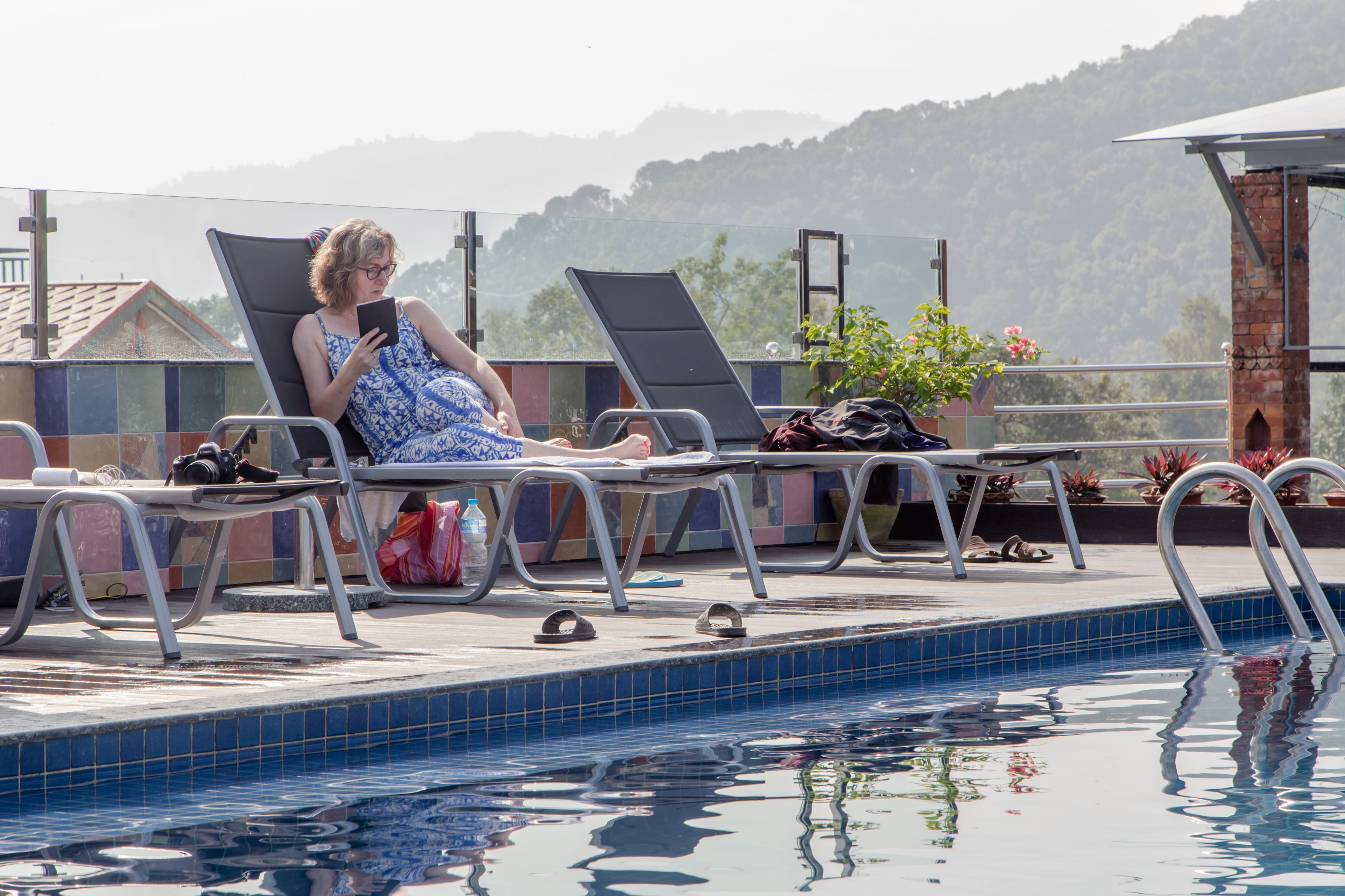 A poolside area with lounge chairs, a pool, and a view of hills.