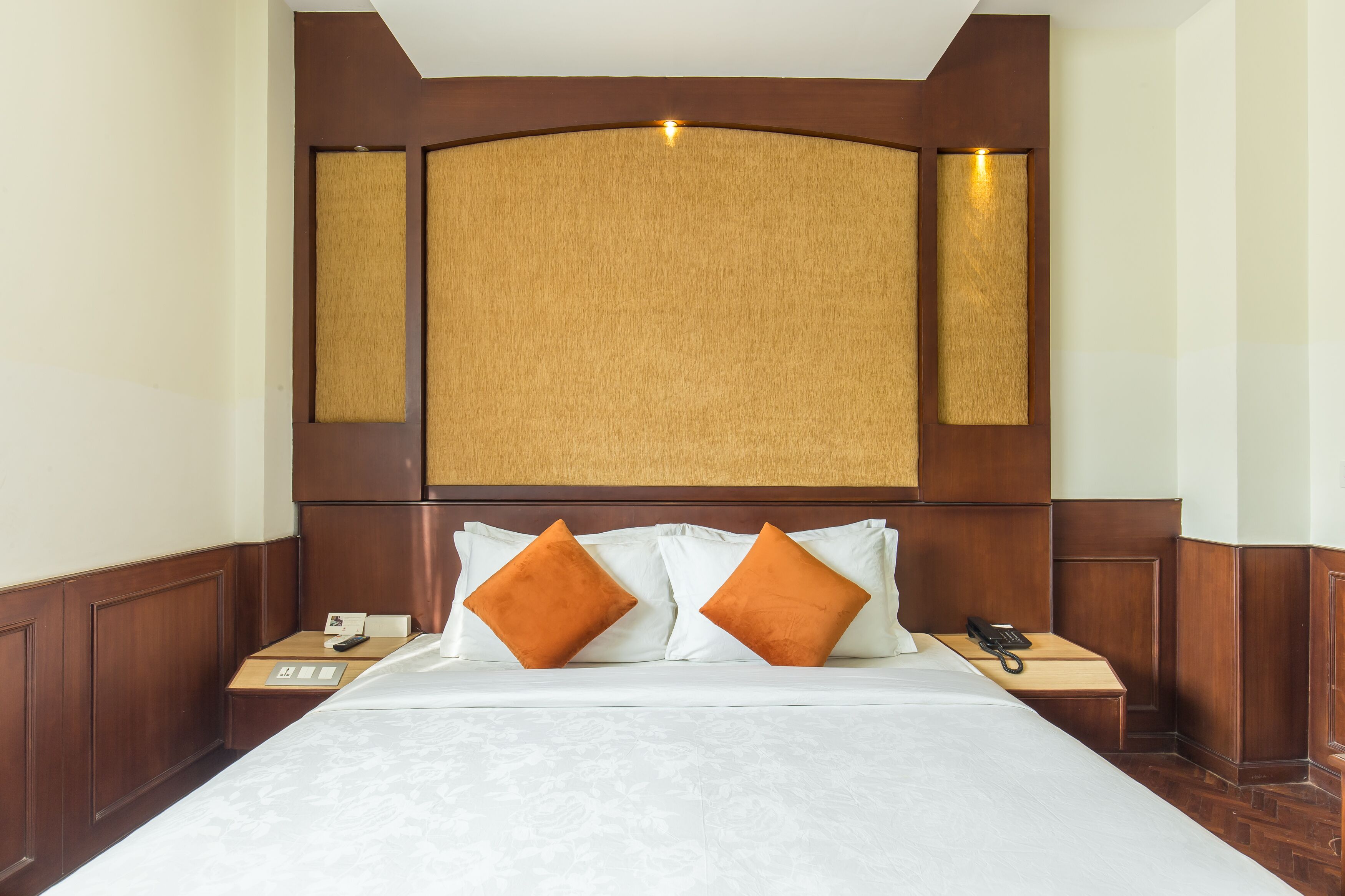 A hotel room with a large bed, two nightstands, a wooden headboard, and a light fixture above the headboard.