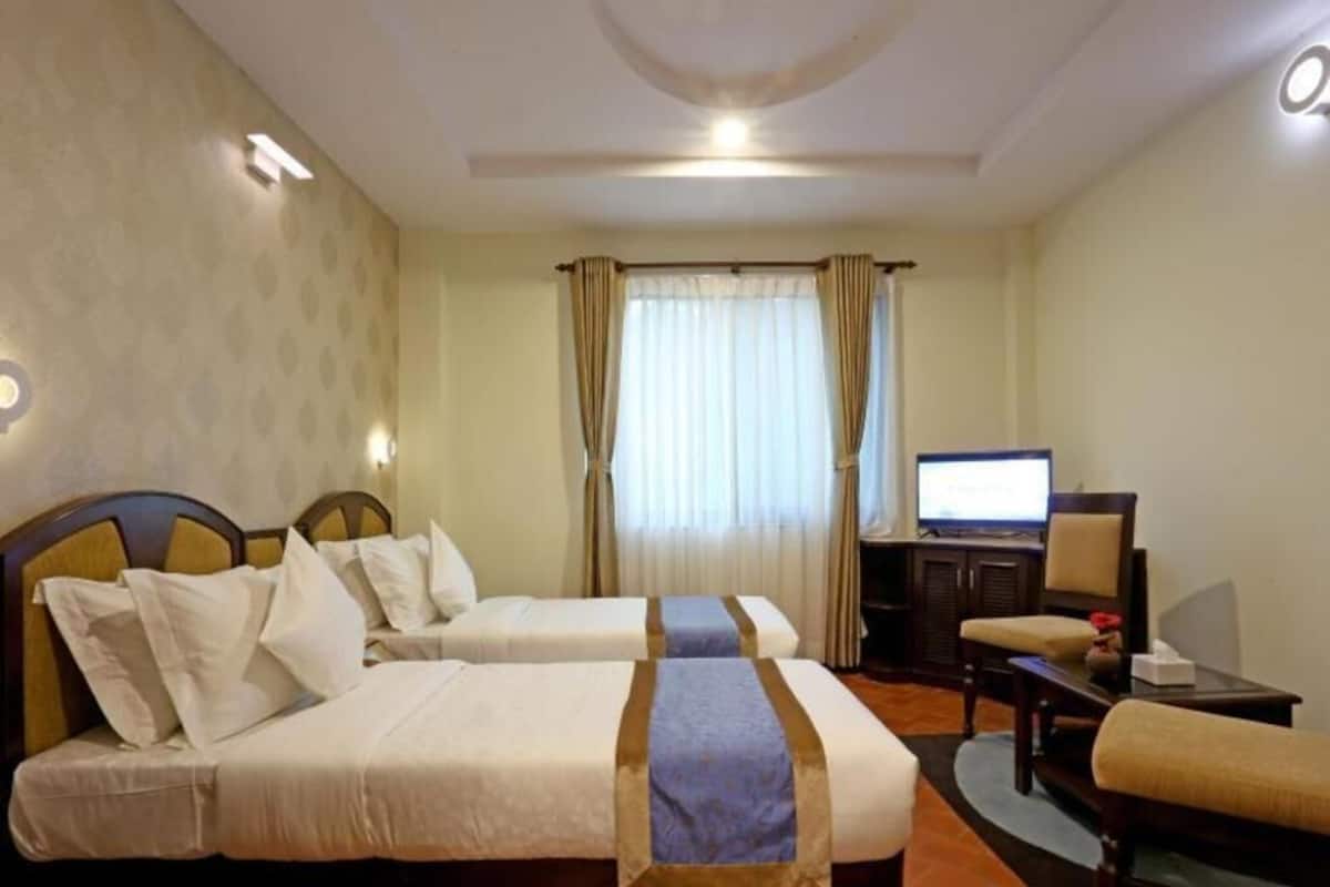 A hotel room with two beds, a desk, a chair, a television, and a window with curtains.