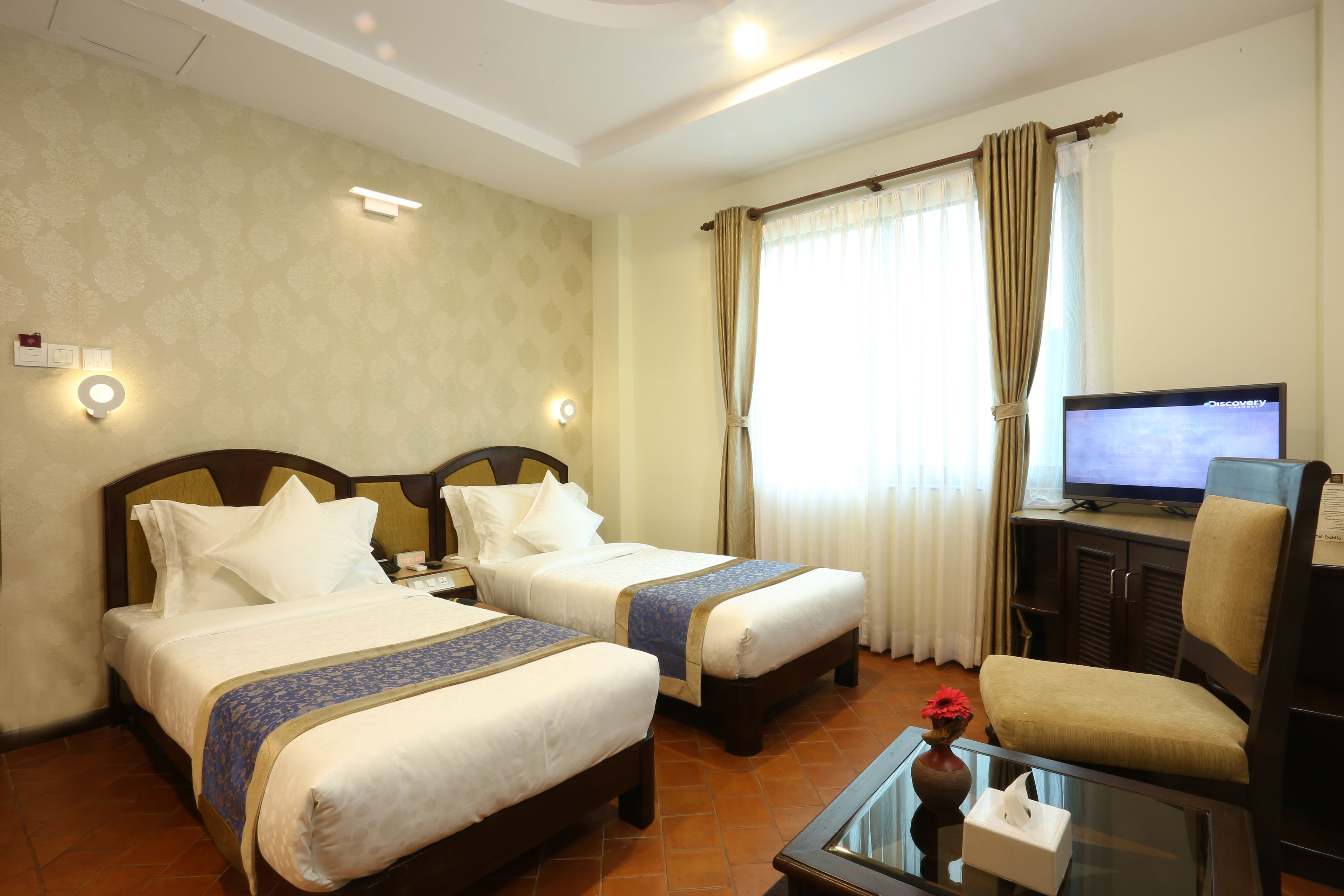 A hotel room with two beds, a television, a glass coffee table, and a chair.