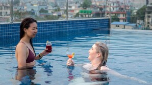 Dos personas en una piscina con un paisaje urbano al fondo.