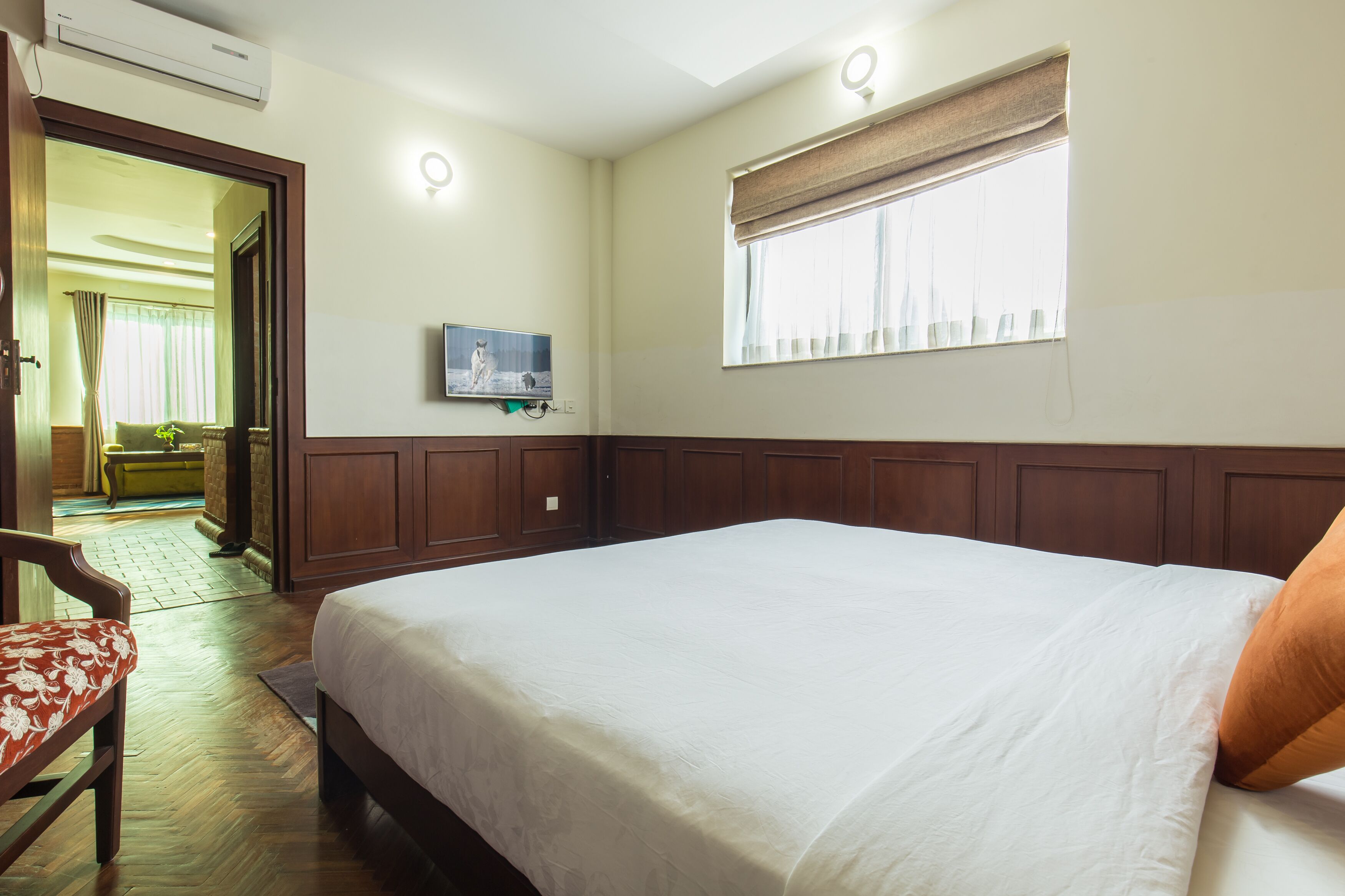 A hotel room with a large bed, a television mounted on the wall, and a window with curtains.