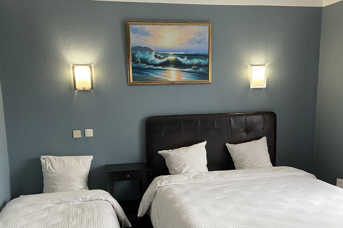 A hotel room with two beds, a dark headboard, and a painting of a sunset over the ocean on the wall.