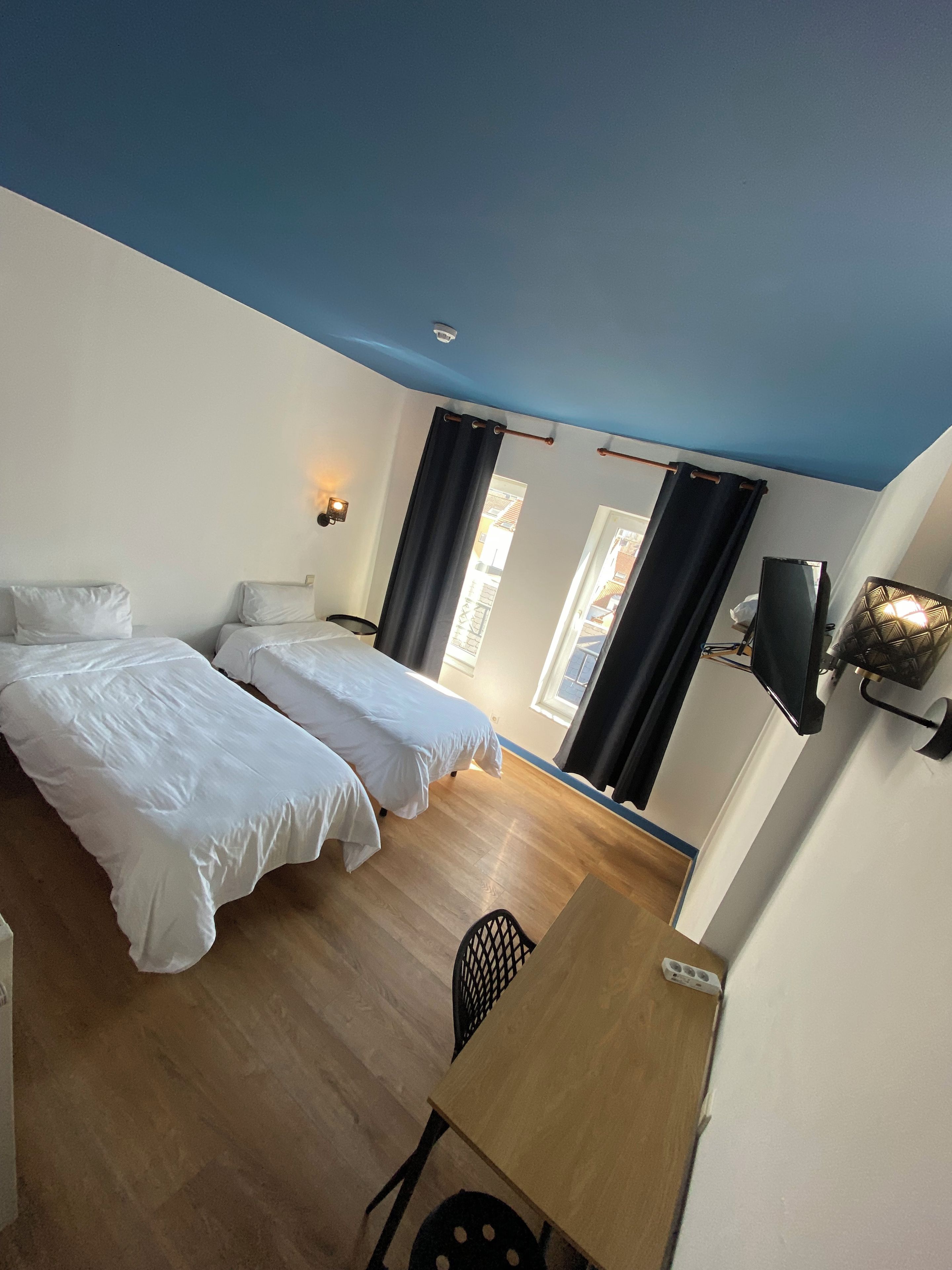 A room with two beds, a desk, a chair, a television, and a window with curtains.