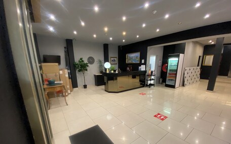 A hotel reception area with a reception desk, a refrigerator, a potted plant, and a clock on the wall.