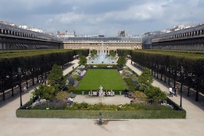 Un imposant bâtiment à l’architecture symétrique, doté d’une fontaine centrale et d’un jardin bien entretenu avec des bancs.