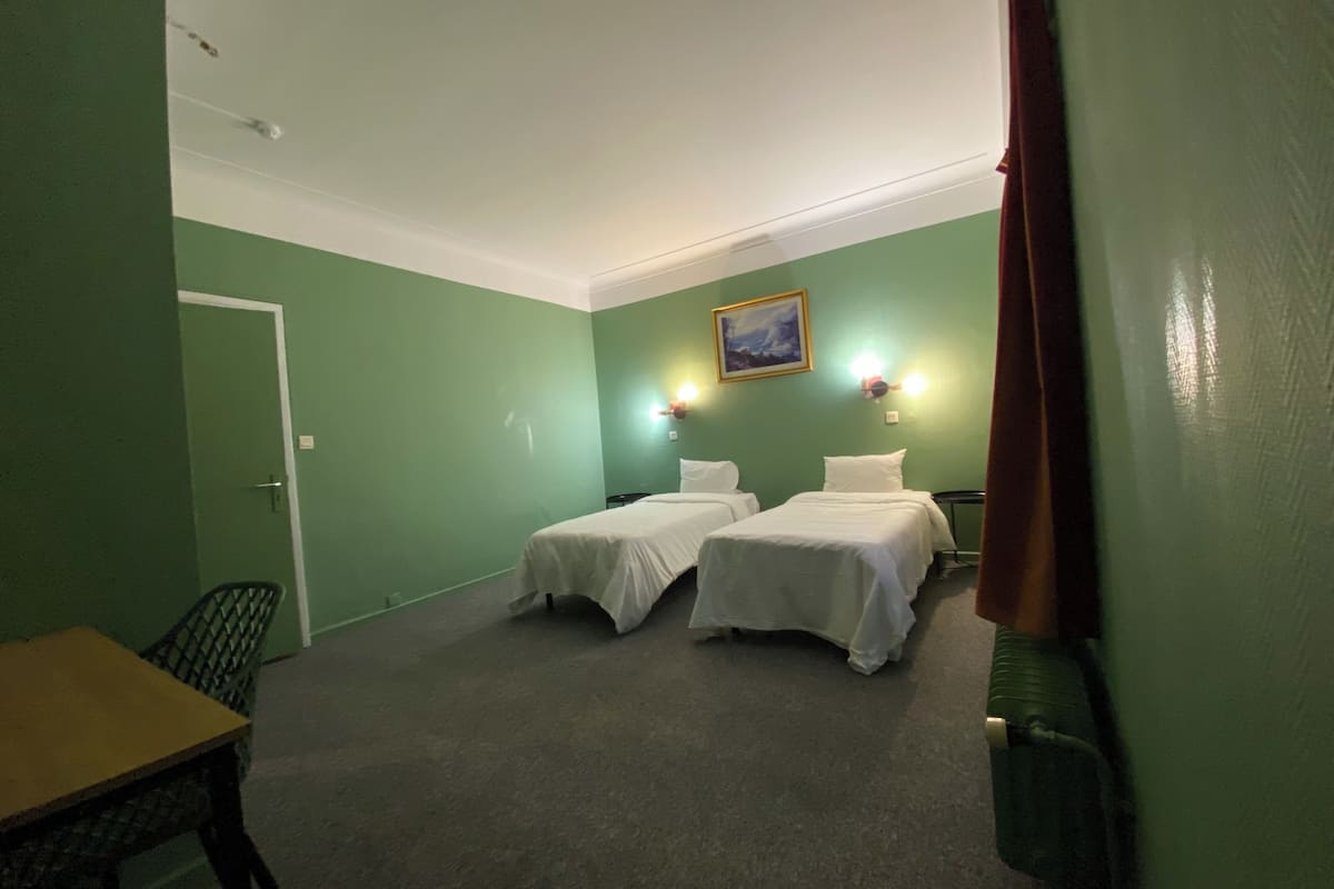 A room with two single beds, a table, and a chair.