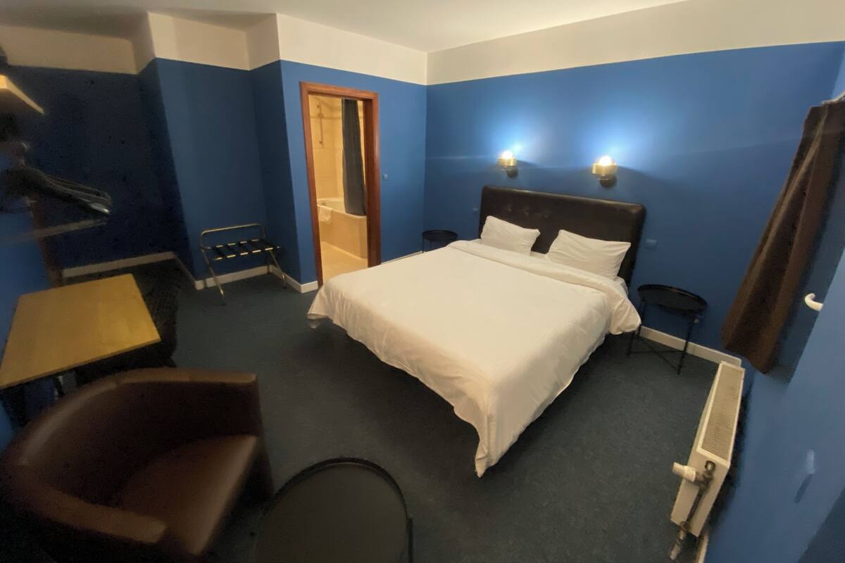 A hotel room with a bed, a chair, a desk, and a bathroom visible through an open door.