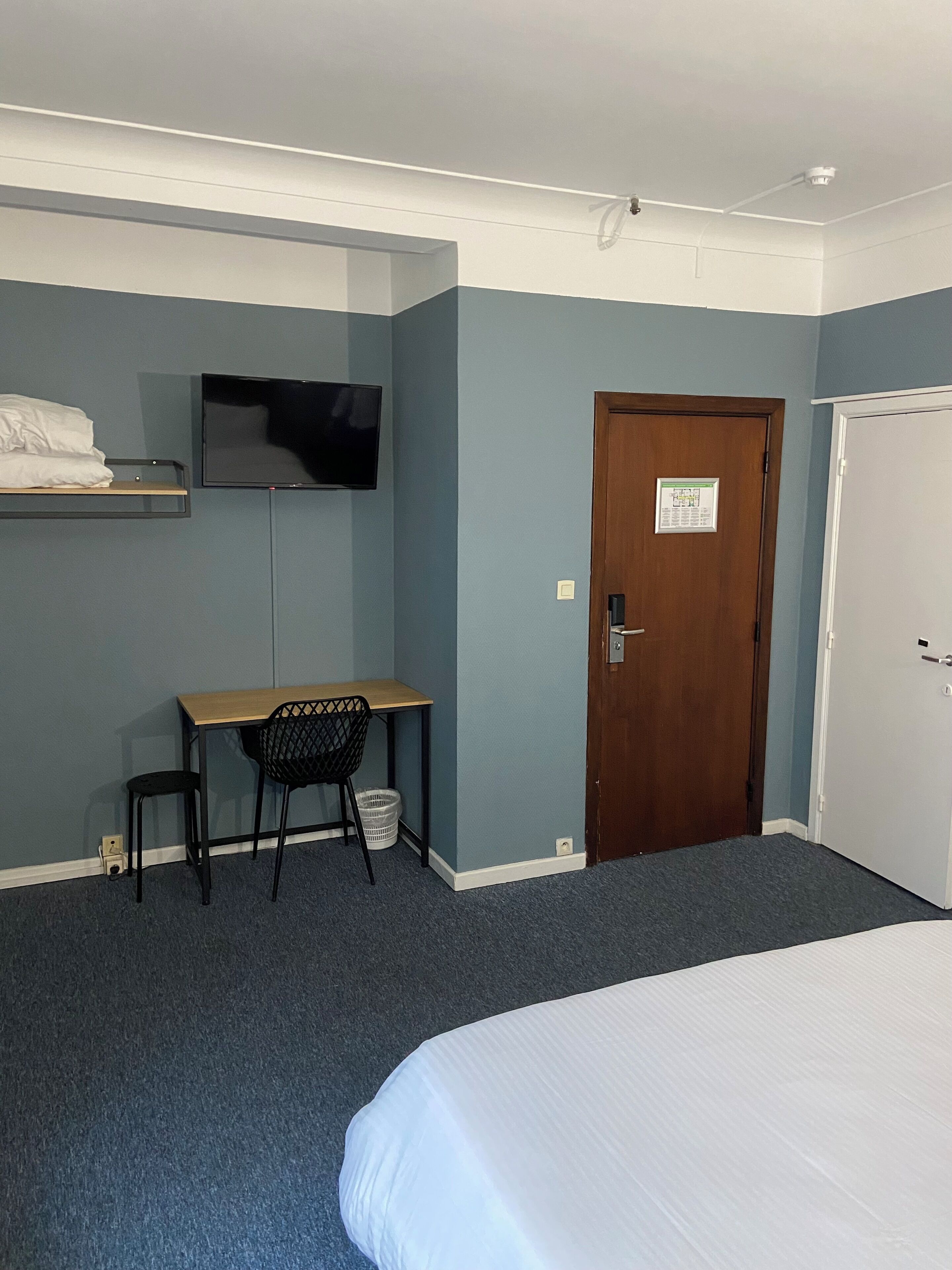 A hotel room with a bed, a desk with a chair, a television, and a door.
