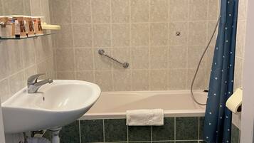 Un baño con lavamanos, bañera y retrete. Hay una toalla colgada del borde de la bañera y una cortina de ducha con un estampado de corazones.