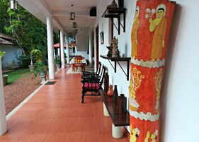 Un pasillo con suelo de baldosas, un banco y una mesa con sillas. Hay elementos decorativos en la pared y una estatua.