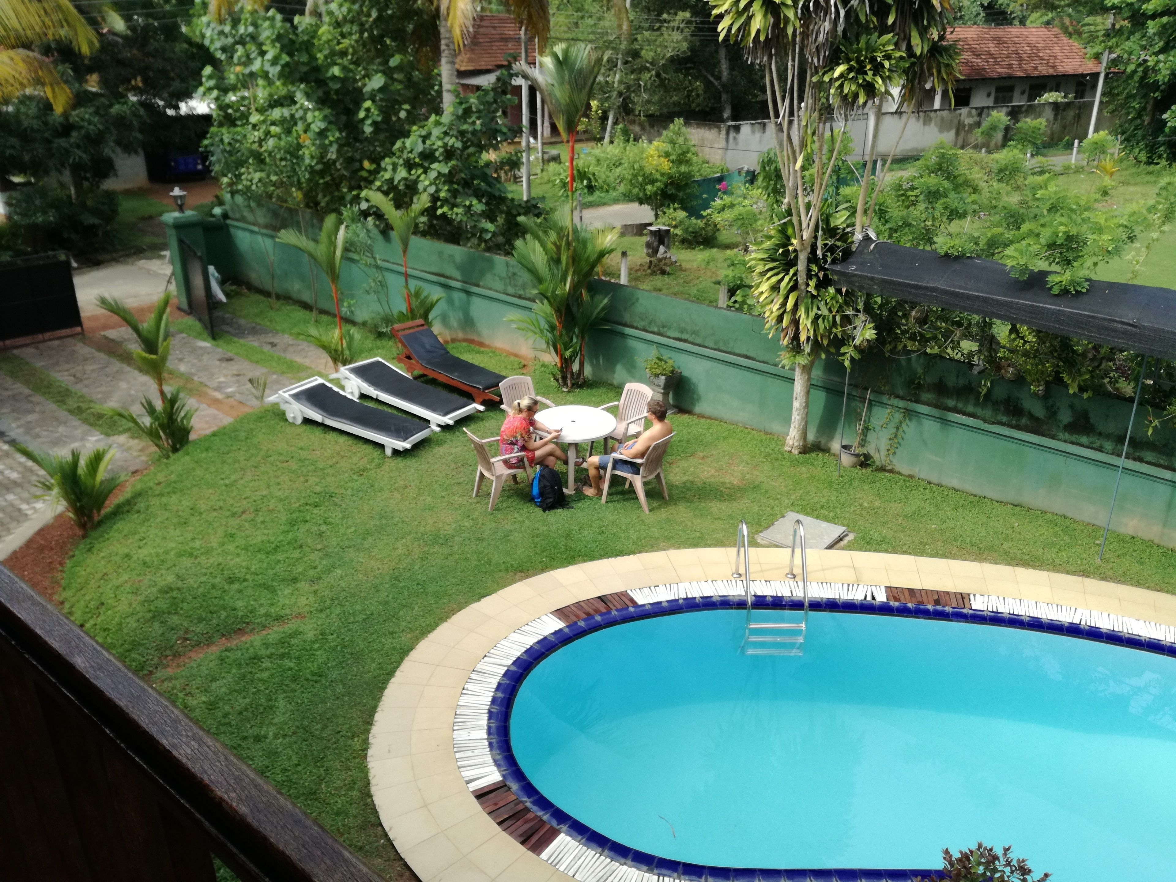 Un patio trasero con piscina, un pequeño césped y algunas sillas de descanso.