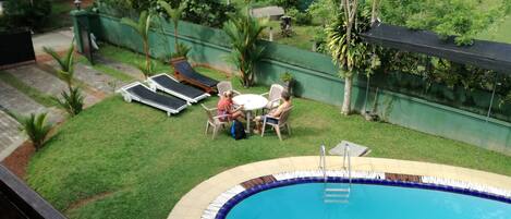Un patio trasero con piscina, un pequeño césped y algunas sillas de descanso.