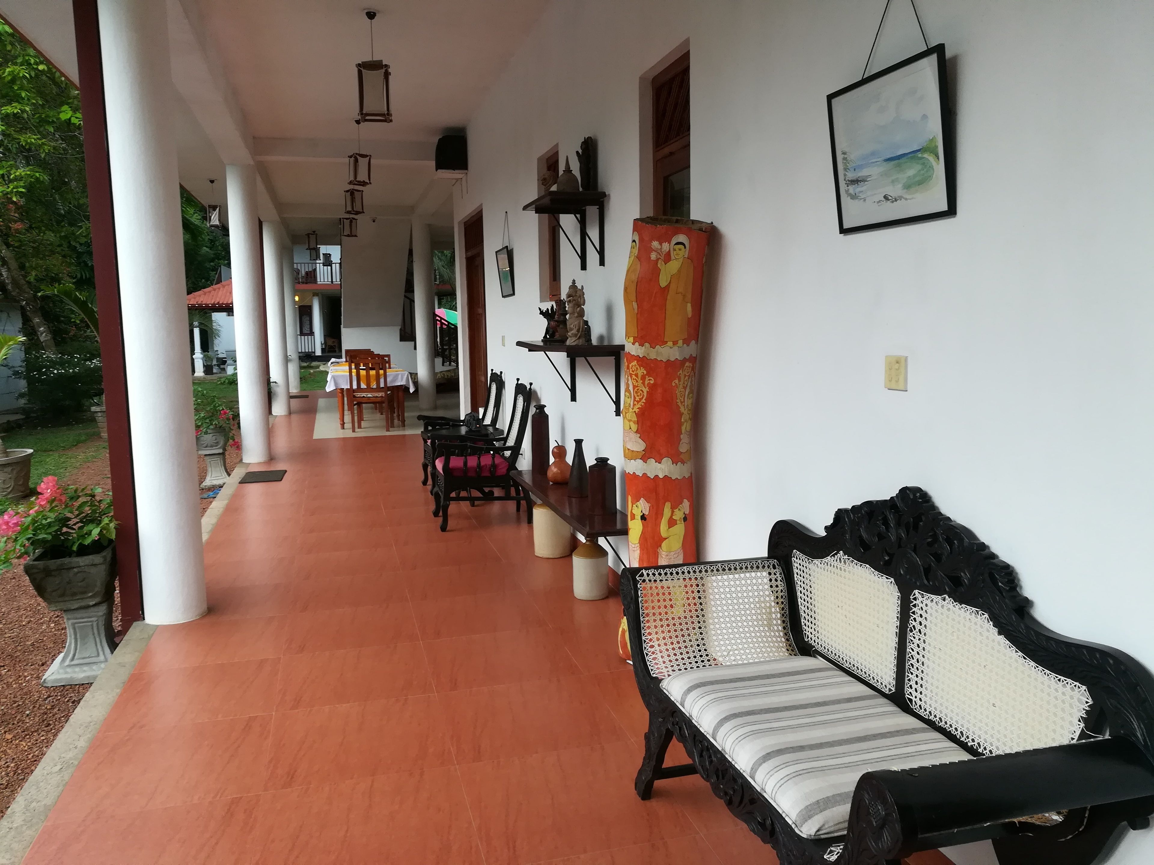 A covered outdoor area with a dining table and chairs, a sofa, and a decorative pillar.