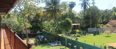 Una piscina con cubierta de madera y vistas a un exuberante jardín con palmeras y una valla verde.