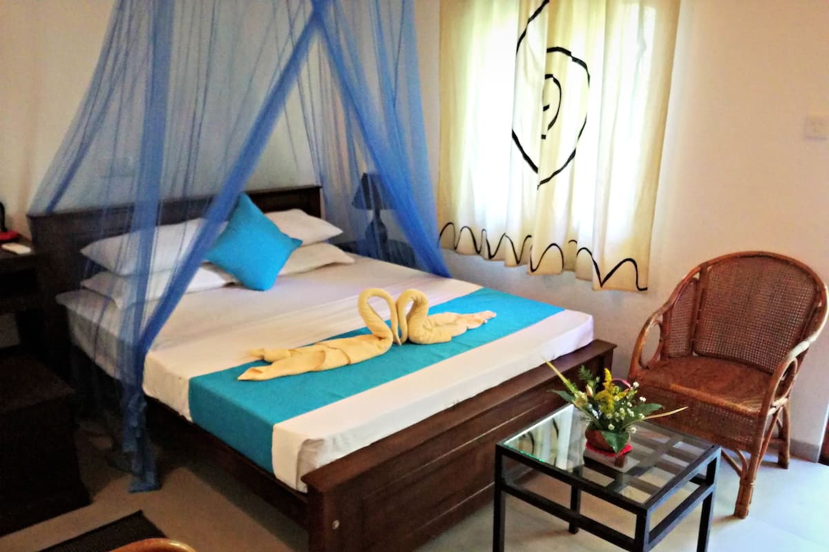 A bedroom with a bed, a chair, and a small table with a vase.