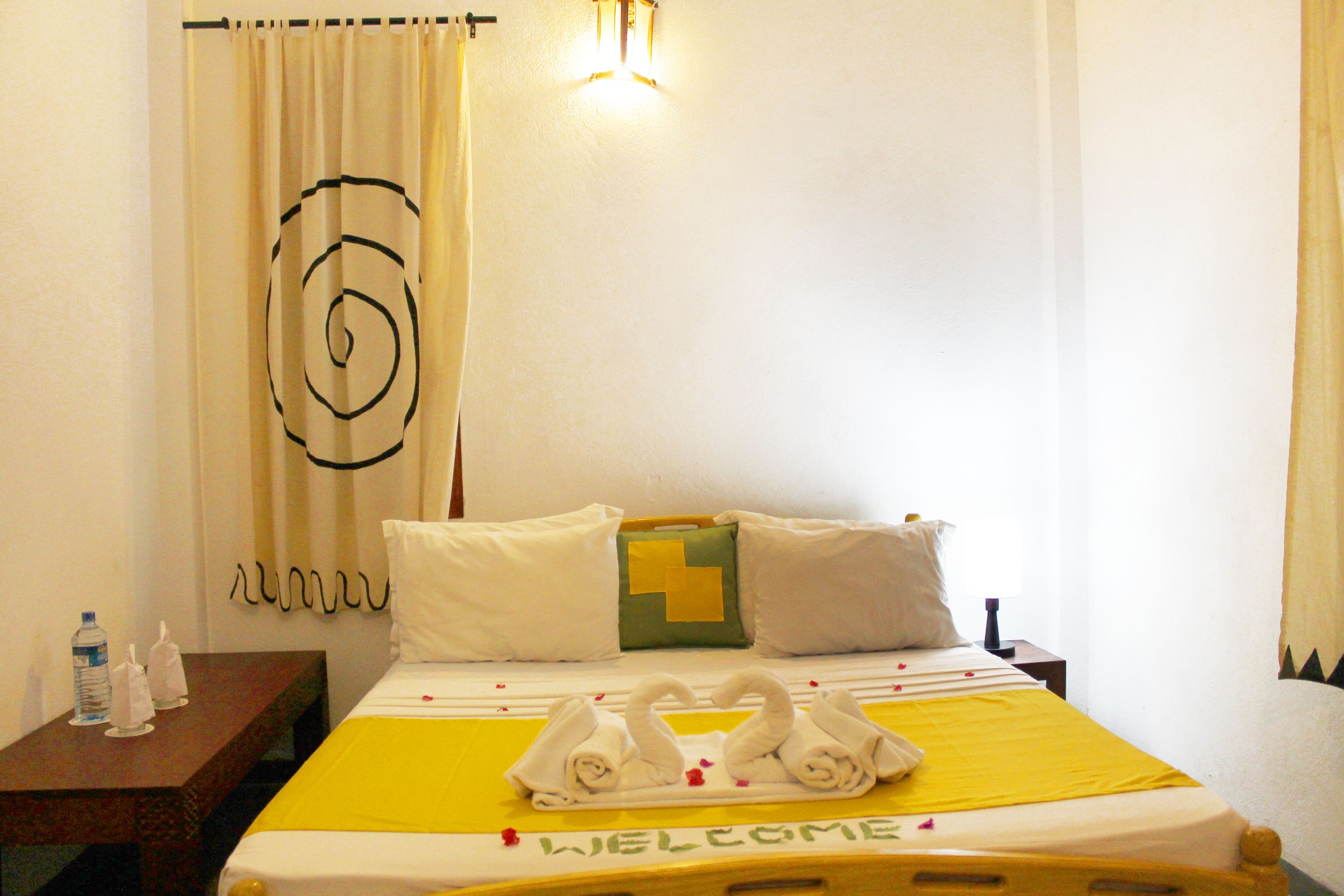 Una habitación de hotel con cama, mesita de noche, botella de agua y toallero.