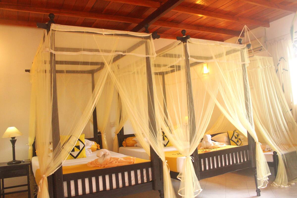 A room with two beds, each with a canopy bedspread and a nightstand with a lamp.