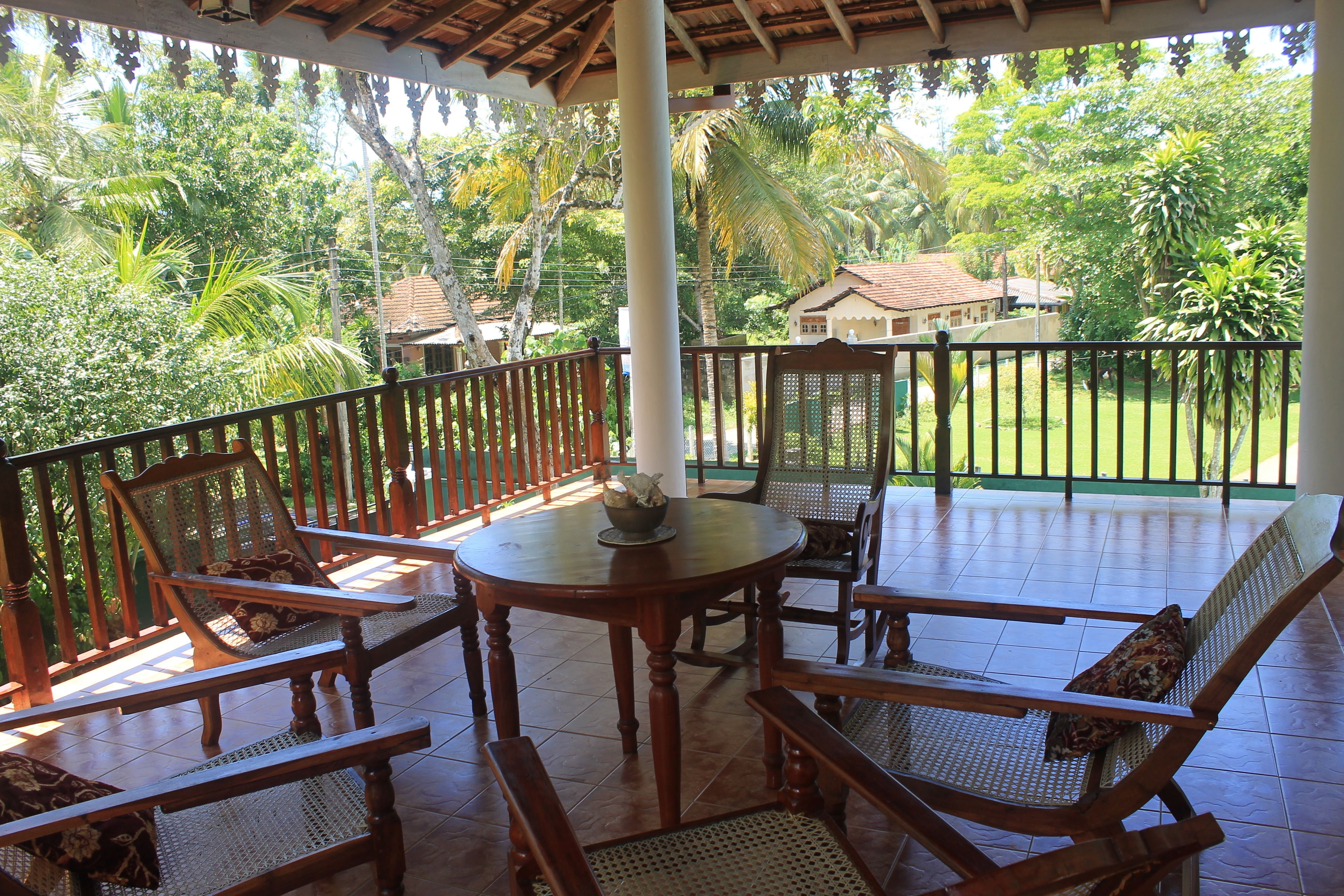 A covered outdoor seating area with wooden furniture and a view of a lush garden.