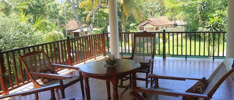 A covered outdoor seating area with wooden furniture and a view of a lush garden.