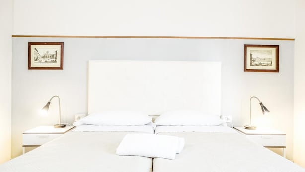 A large bed with a white headboard, two bedside tables with lamps, and framed pictures on the walls. - Iris Florentina (Florence)