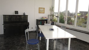 A room with a piano, a white table, and chairs. There is a window with a view of the outside. - Iris Florentina (Florence)