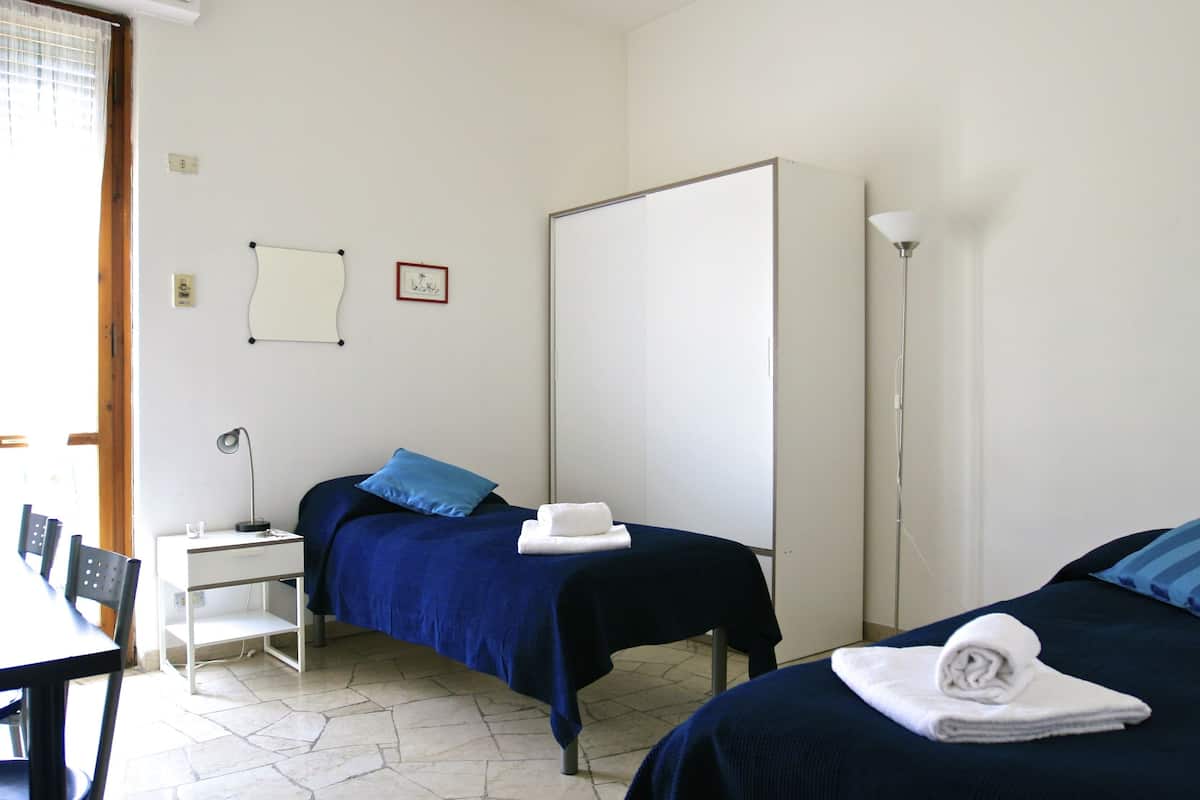 A hotel room with two beds, a desk, a chair, a lamp, and a whiteboard on the wall.