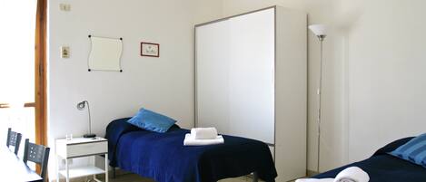 A hotel room with two beds, a desk, a chair, a lamp, and a whiteboard on the wall.