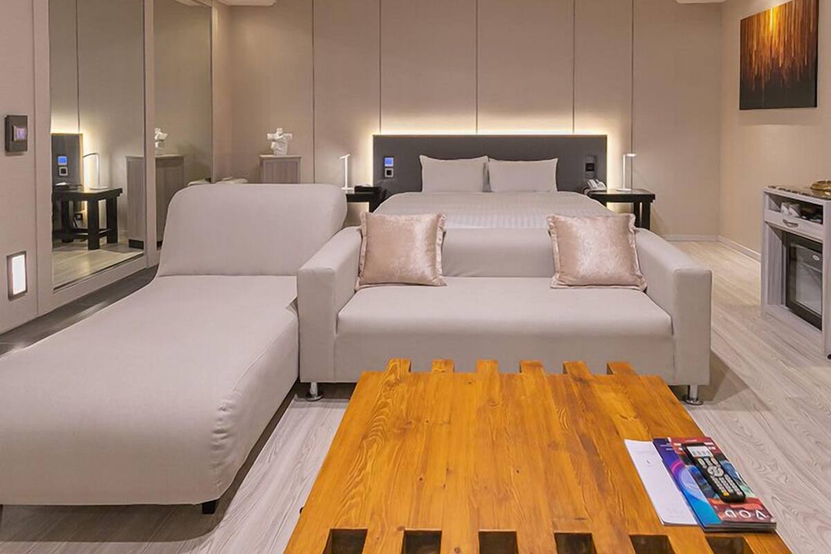 A modern hotel room with a large bed, a sofa, a wooden coffee table, and a large mirror.