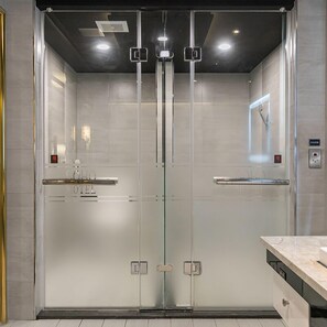 A modern elevator with glass doors, control panel, and emergency light.