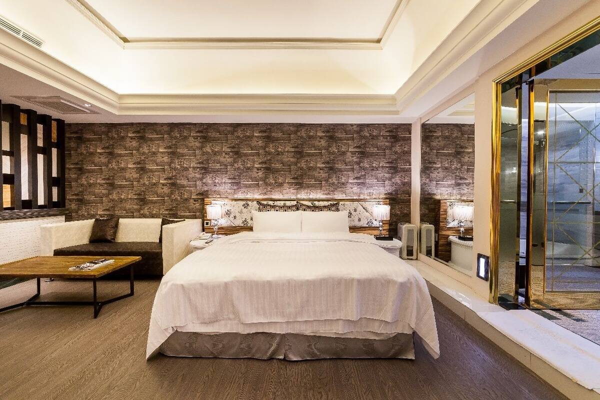 A hotel room with a large bed, a sofa, a coffee table, and a view of the city through a glass door.
