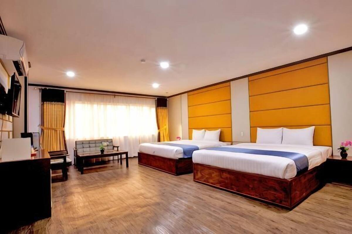 Habitación de hotel con dos camas, un escritorio, una silla, un sofá y un ventanal con cortinas.