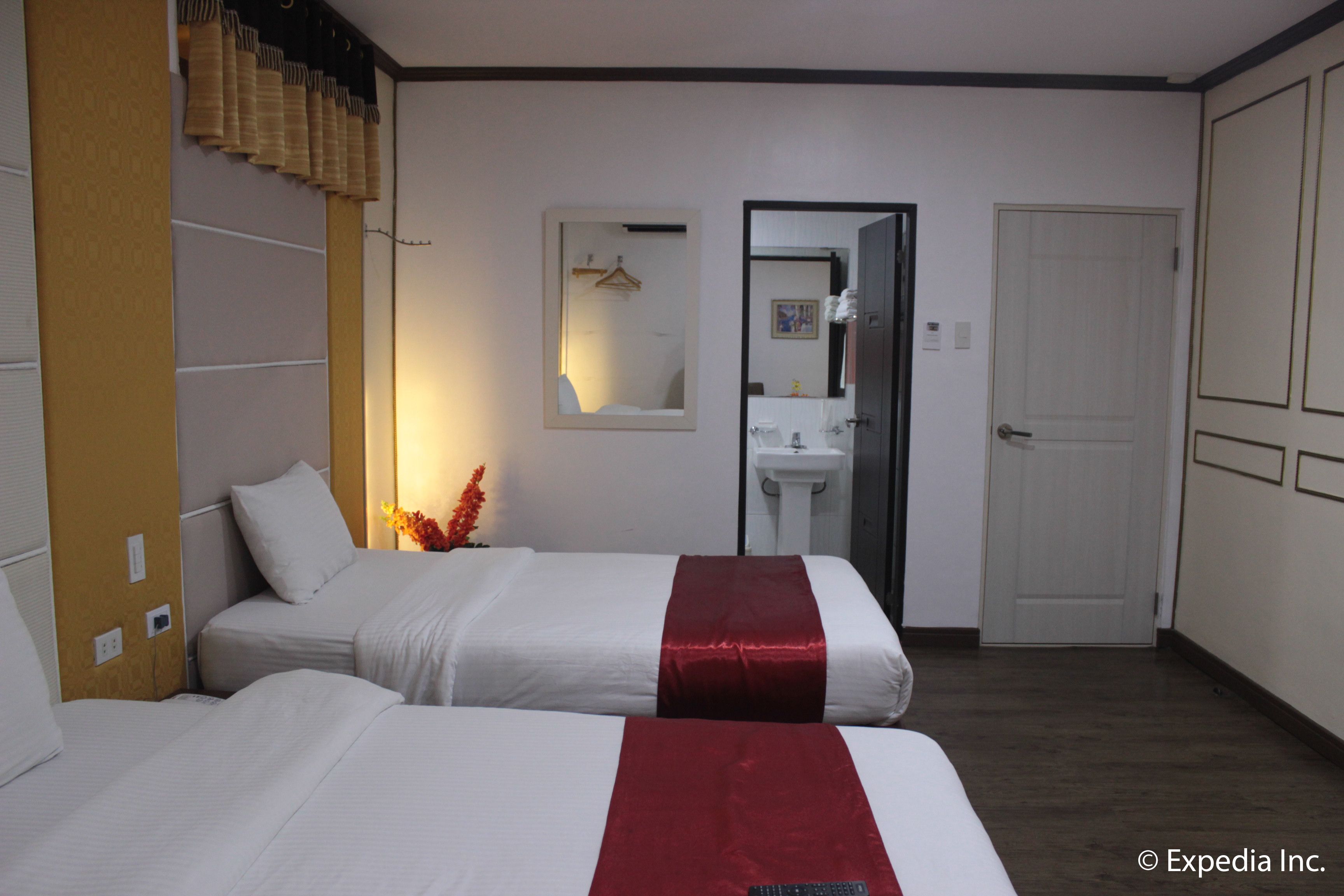 A hotel room with two beds, a white and red bedspread, a mirror, a sink, and a wardrobe.