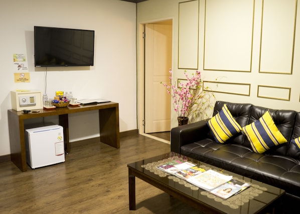 A living room with a leather sofa, a coffee table, a desk with a computer, a television, and a small refrigerator. - Horizon Hotel (Olongapo)