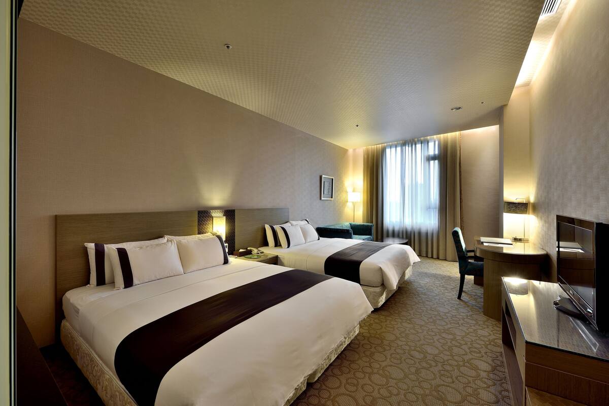 A hotel room with two beds, a desk, a chair, and a television.
