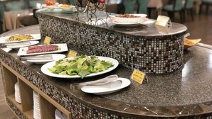 Un mostrador de buffet con diversos platos, incluyendo una ensalada y un guiso de carne, en un restaurante.