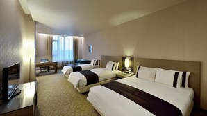 Una habitación de hotel con tres camas, un escritorio, un televisor y una ventana con cortinas.