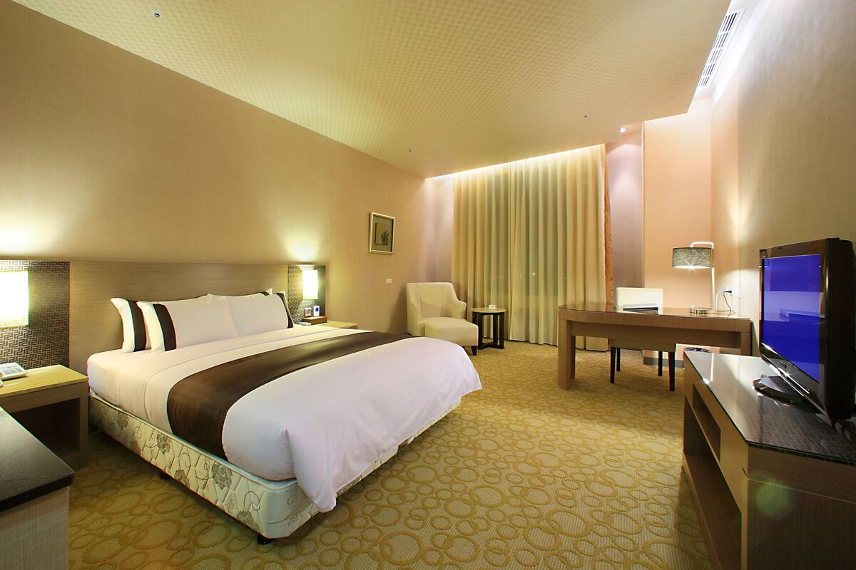 A hotel room with a large bed, a desk, a chair, a television, and a small table.