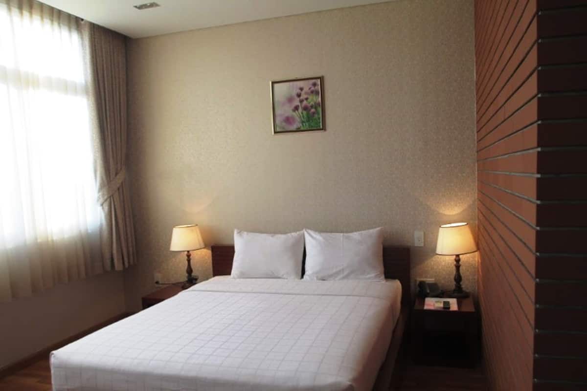 A hotel room with a large bed, two bedside lamps, a framed floral picture on the wall, and a window with curtains.